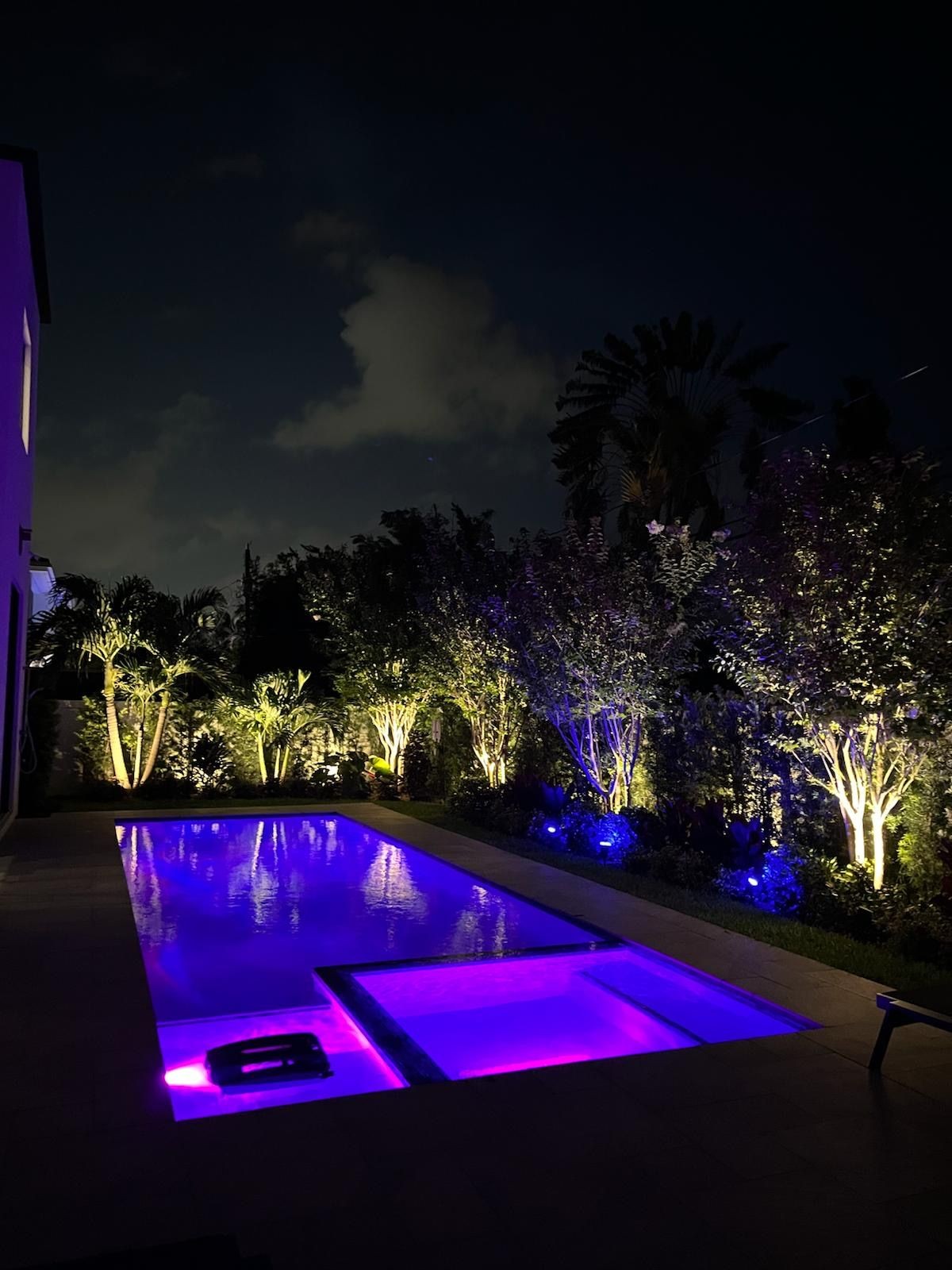 Luxury backyard pool and garden illuminated with warm white and purple LED landscape lighting in Jupiter, Florida